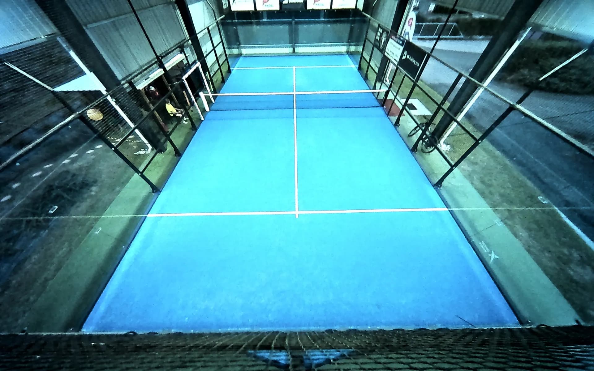 Prázdný kurt Padel Klatovy z pohledu kamery nad zadní stěnou za denního světla